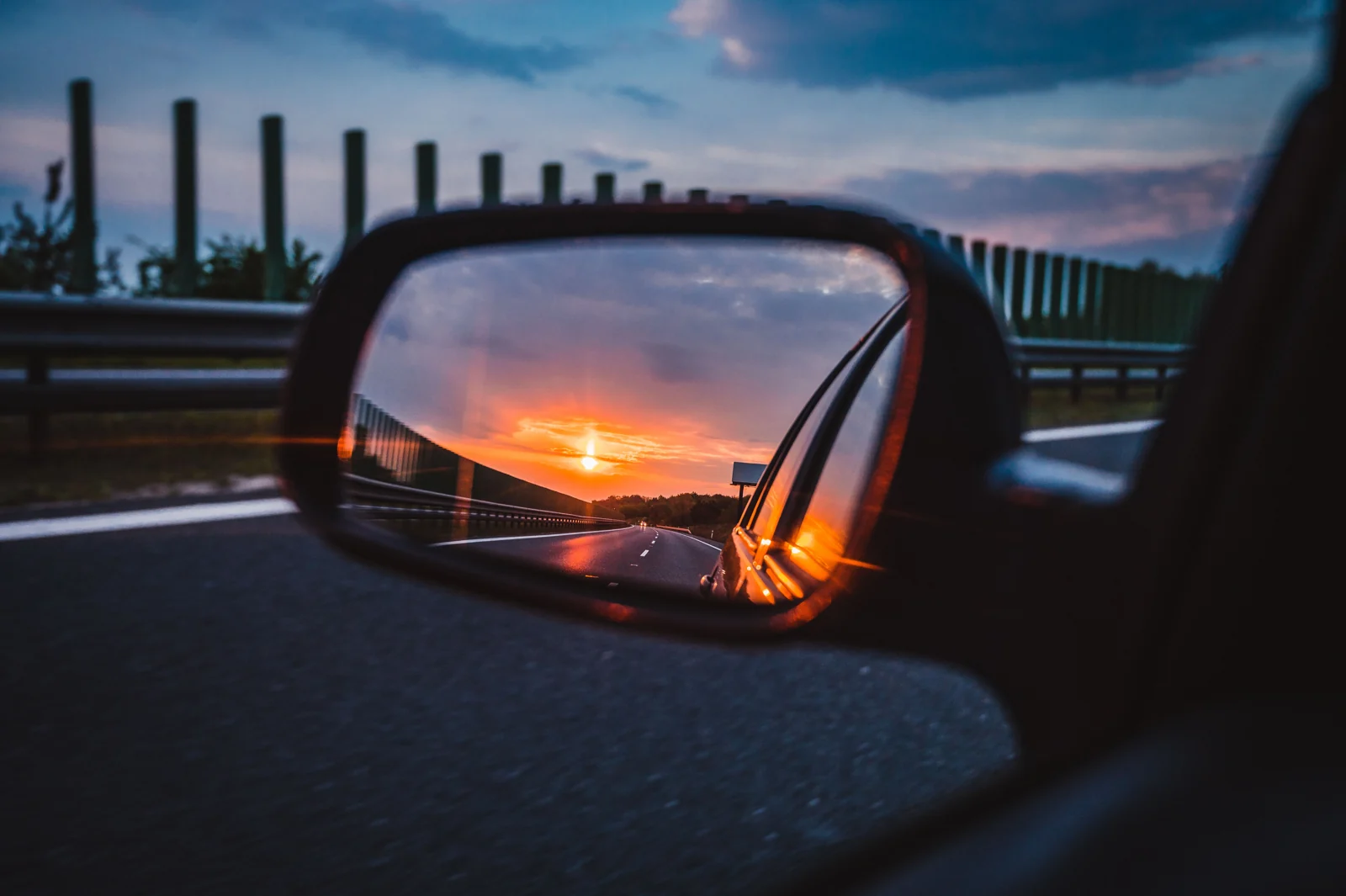 Redaktionellt fotografi av kvällsljus och en väg som speglas i en bils sidospegel.